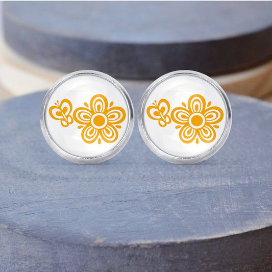 A pair of round stud earrings featuring a butterfly Pyrex printed design, displayed on a grey wood surface.