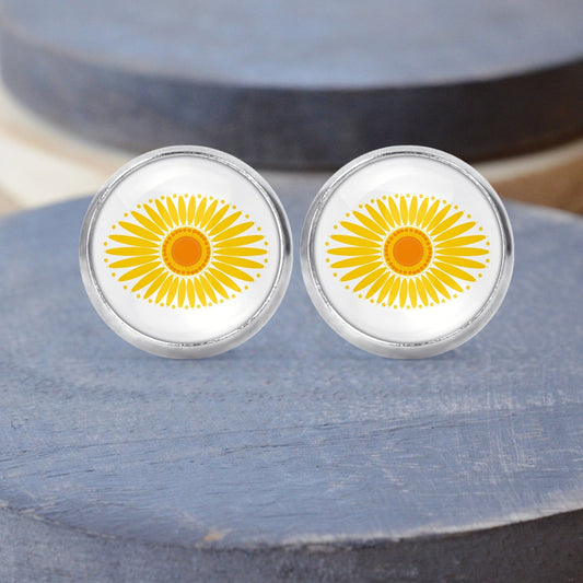 A pair of yellow and white daisy print pyrex stud earrings displayed on a gray wood surface.