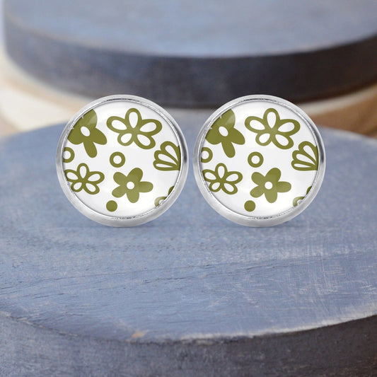 A pair of stud earrings featuring green and white Spring Blossom Pyrex pattern, set in silver-colored post settings, displayed on a gray platform.