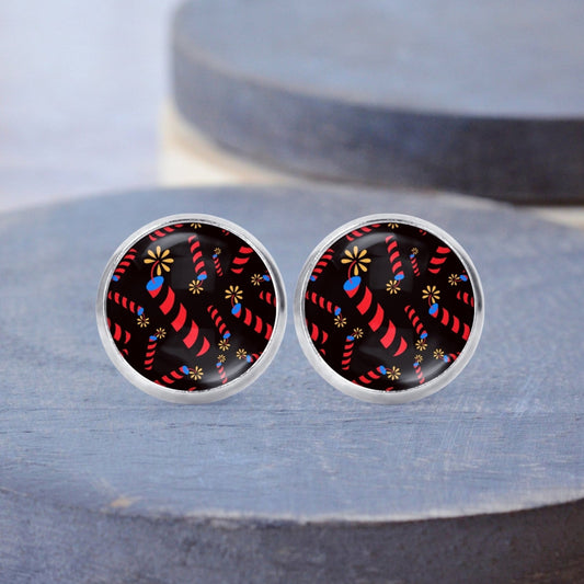 Round surgical steel stud earrings with black background and firecracker pattern on a wood backdrop.